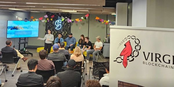 A speaker and seated participants at a Virginia Blockchain Council community gathering, with the council banner in the foreground