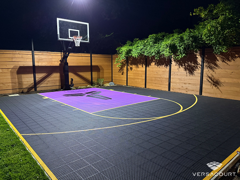 Illuminated backyard basketball court with purple and charcoal game areas