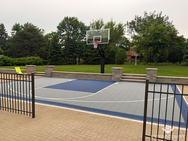 Blue and gray VersaCourt basketball court adjoining a brick patio and green lawn